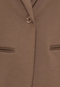 Blazer marron avec un seul bouton marron fermé et deux poches fentes horizontales de chaque côté.