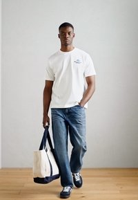 Valge puuvillane T-särk väikese sinise graafikaga, helesinised teksad, mustad spordijalatsid ja beež käekott siniste aktsentidega.