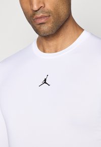 Hvid kortærmet træningsshirt lavet af glat stof, med et lille sort Air Jordan-logo på brystområdet.