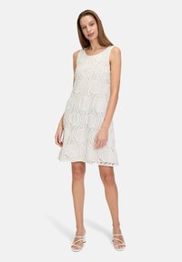 Weißes Spitzenkleid mit kreisförmigen Mustern und ärmellosem Design. Akzentuiert mit zarten Texturen und einem ausgestellten Saum.