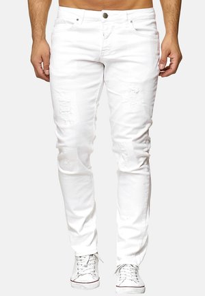Jeans blancos desgastados que presentan un ajuste slim, diseño de cinco bolsillos y cierre de botón. Combinados con zapatillas blancas para un contraste.