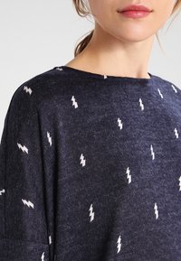 Haut à manches courtes bleu marine en tissu doux, avec un motif de foudre répété en blanc sur le t-shirt. Design classique à col rond.