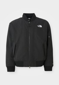 Veste bomber noire en tissu lisse, avec un col rond, des poignets côtelés et des poches latérales zippées. Le logo The North Face est sur la poitrine.