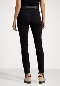 Svarta denim skinny jeans med medelhög midja, med en slät textur, två bakfickor och ett svart bälte. Bärs med kilklackssandaler.