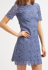 Vestido de manga corta en encaje lavanda con patrón de flores y detalles recortados, con un dobladillo recto y tejido texturizado.