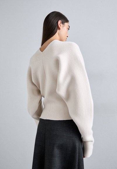 Krēmkrāsas adīts džemperis ar apjomīgām piedurknēm un V-veida kakla izgriezumu, savienots ar tumšu, strukturētu svārku.