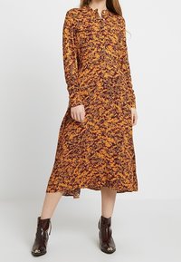 Abito midi a maniche lunghe arancione con motivo astratto nero, realizzato in un tessuto leggero, con colletto button-down e vestibilità comoda.