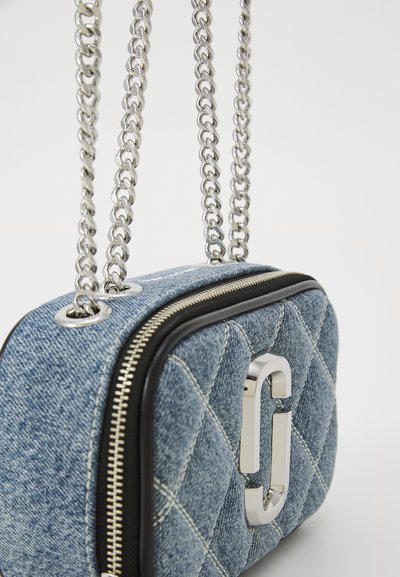 Denim crossbody bag with quilted texture, silver hardware, a front logo detail, and dual chain straps for carrying.