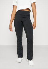 Schwarze Fitnesshosen mit hoher Taille, glatter Textur und horizontalen Streifen auf den Oberschenkeln. Kombiniert mit einem kurzen, weißen Crop-Top.