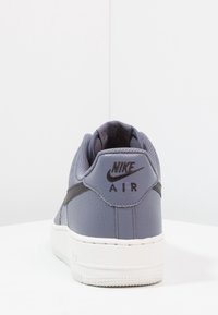 Szare skórzane sneakersy z teksturowaną powierzchnią, białą gumową podeszwą i czarnym logo Nike na pięcie. Posiadają wyściełany kołnierz dla wygody.