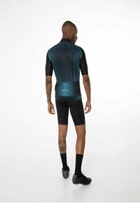 Cyklistický dres v tmavě modré barvě s geometrickými vzory, krátkými rukávy a kapsami na zádech, v kombinaci s černými cyklistickými kraťasy a botami.