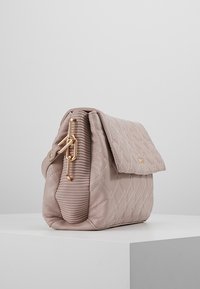 Quiltet lysebrun håndtaske med en fold-over flap, der har en lås i guldfarvet kæde og ribbet sidetextur. Elegant syning gennem hele tasken.