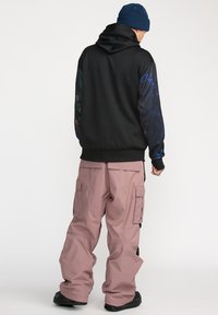 Felpa nera con maniche a motivo colorato, abbinata a pantaloni cargo rosa larghi con molte tasche. Calzature nere completano il look.