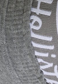 Grå tygkeps med en texturerad yta, med vit broderad text på ena sidan och en slät yta på den andra.