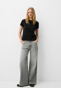 Black short-sleeve t-shirt paired with wide-leg gray jeans. The t-shirt has a smooth texture, while the jeans feature a faded wash and visible stitching.