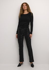 Zwarte longsleeve top met gerimpeld detail, gecombineerd met zwarte broek met een textuur van slangenpatroon, afgewerkt met zwarte hakken.