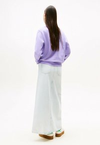 Felpa lavanda, vestibilità rilassata, abbinata a una lunga gonna di jeans azzurro chiaro. Scarpe platform marroni notevoli e accenti verdi visibili.