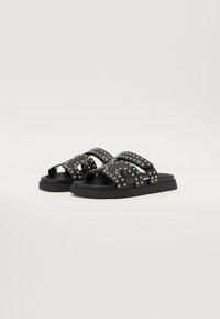Schwarze Rutschesandalen mit strukturierten Riemen, die mit silbernen Nieten verziert sind, einer flachen Gummisohle und einem offenen Zehendesign.