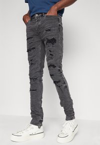 Slim-fit svarta jeans med slitna detaljer och fransade lappar, kombinerat med vita höglate sneakers.