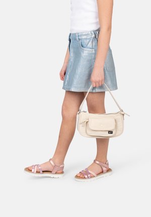 Bolso beige con cierre de cremallera y bolsillo frontal, sostenido en la mano. Falda mini metálica plateada y sandalias ligeras de tiras rosas con suelas blancas.