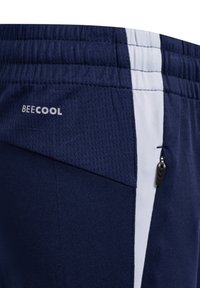 Gros plan d’un short de sport bleu marine avec une bande verticale blanche, une poche zippée et "BEECOOL" imprimé sur la ceinture en tissu en maille.