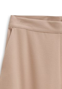Beige Hose mit einer weichen, strukturierten Oberfläche, ausgestattet mit einem breiten Bündchen und seitlichen Taschen. Das Design ist schlicht und klar.