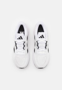 Baskets blanches avec des accents noirs, tige en maille et lacets plats. Présente un logo à trois rayures sur la languette et une texture perforée sur les côtés.