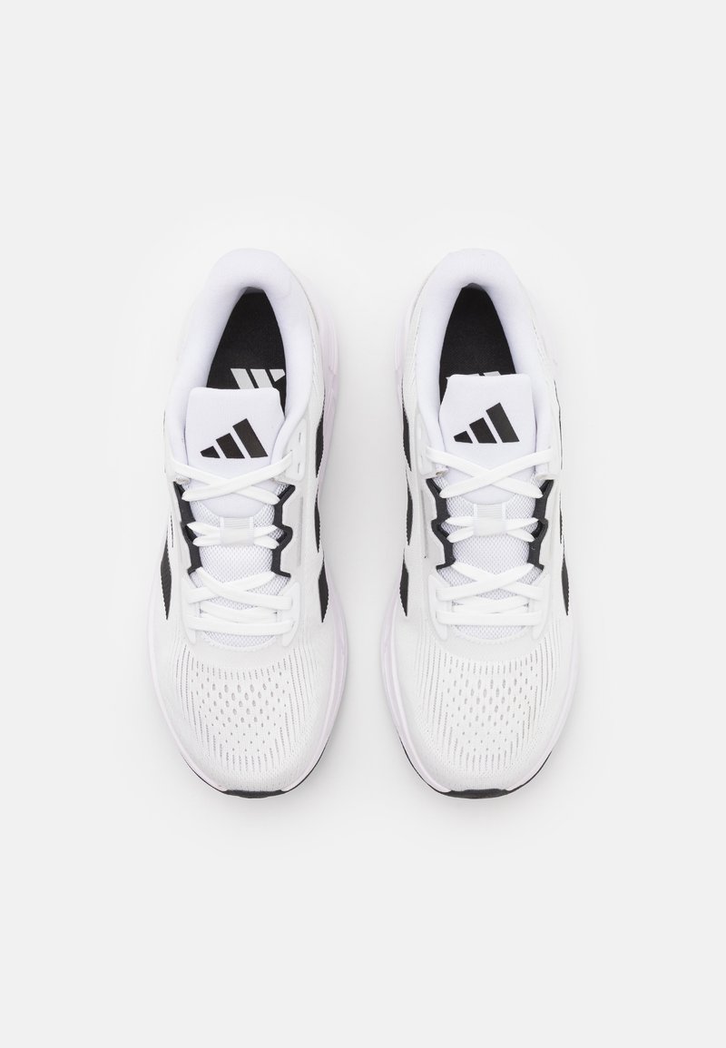 Baskets blanches avec des accents noirs, tige en maille et lacets plats. Présente un logo à trois rayures sur la languette et une texture perforée sur les côtés.