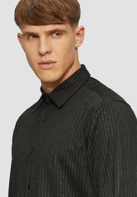 Zwarte shirt met een kraag, voorzien van subtiele verticale strepen, lange mouwen en een soepele textuur. Met knopen aan de voorkant en een getailleerde pasvorm.