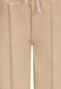 Beige broeken van zachte, rekbare stof met een tailleband met trekkoord en verticale naden voor extra textuur.