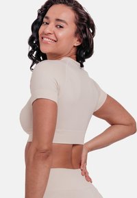 Light beige, short-sleeved crop top with a fitted design. Features a curved hem and a subtle ribbed texture on the fabric.
