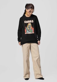 Czarny sweatshirt z kolorową grafiką przedstawiającą czaszkę oraz napisem "Ghouls Just Wanna Have Fun". W połączeniu z beżowymi spodniami o szerokim kroju.