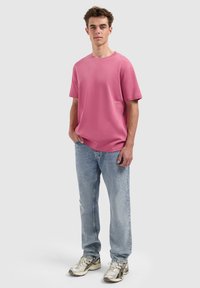 Roze T-shirt met korte mouwen, een ronde hals en een relaxte pasvorm. Draag het met lichtblauwe spijkerbroeken en zilveren sneakers. Minimale merkdetails zichtbaar.