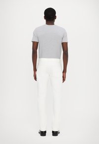 Gray short-sleeve t-shirt, paired with white pants, featuring a slim fit, smooth texture, and black shoes, viewed from the back.
