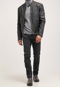 Chaqueta de cuero negra con hombros acanalados, cuello alto gris, pantalones ajustados oscuros y botas negras. Textura suave, diseño minimalista.