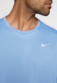 Világoskék sportpóló kerek nyakkivágással, texturált anyagból, bal mellrészen egy kis fehér Nike logóval.