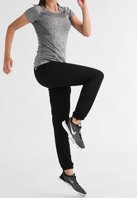 Grijze sport T-shirt van textuurstof, gecombineerd met zwarte joggingbroeken. Zwarte sneakers met witte accenten maken de outfit compleet.