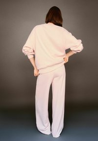 Felpa oversize rosa chiaro con spalle scese; pantaloni a gamba larga abbinati. Tessuto morbido e strutturato, vestibilità ampia. Design minimalista.