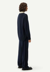 Marinblå tröja med ribbad nederkant och ärmslut, tillsammans med matchande vida byxor. Tyget verkar mjukt, med en kontrasterande ljus krage.