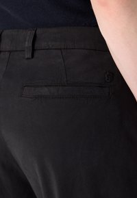 Pantalons noirs avec une texture lisse, une poche arrière avec une couture discrète, et un petit logo près de la taille.