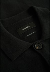 Sweater negro de punto con cuello camisero, que presenta un botón negro y una etiqueta de marca con el texto "GABBA" y "COMPACT KNIT".
