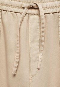 Beige katoenen joggingsbroeken hebben een elastische tailleband, een trekkoord en een voorzak met subtiele stikseldetails.