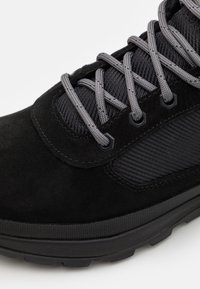 Chaussure de randonnée noire avec des panneaux en tissu texturé gris, des lacets ronds gris et une semelle extérieure en caoutchouc noire avec motif de crampons.