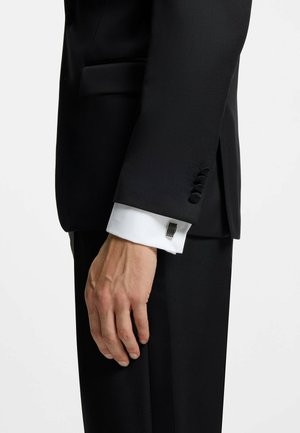 Czarna marynarka z fakturowanym wykończeniem, z białym mankietem, ozdobnymi guzikami oraz widocznymi przeszyciami na mankiecie i boku marynarki.