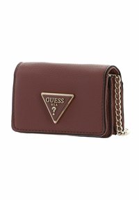 Portafoglio marrone dalla texture particolare con un logo "GUESS" triangolare in tonalità oro. Presenta una tracolla a catena e bordi cuciti per un dettaglio raffinato. Design compatto.