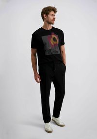 Zwarte t-shirt met een grafische print in rood, geel en grijs, gecombineerd met zwarte broek en witte sneakers. Casual pasvorm.