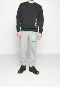 Svart sweatshirt med Nike-logotyper, ovanpå en grön skjorta. Grå sweatpants med flera Nike-logotyper. Svarta sneakers med gummisålar.