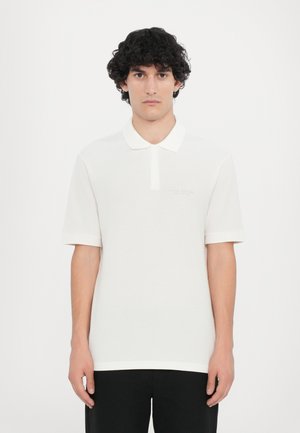 Hvit polo skjorte med klassisk krage og korte ermer. Myk tekstur, med en subtil logo på brystet. Kombinert med mørke bukser.