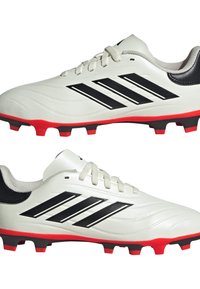 Botas de fútbol blancas con rayas negras, suela roja y parte superior texturizada. Presentan un diseño con cordones y un collar acolchado para mayor comodidad.