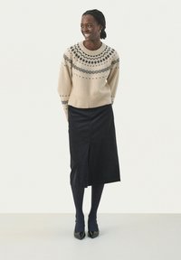 Pull en tricot beige avec un motif marine, associé à une jupe en velours côtelé noire avec une fente à l'avant. Porté avec des collants noirs et des talons noirs.